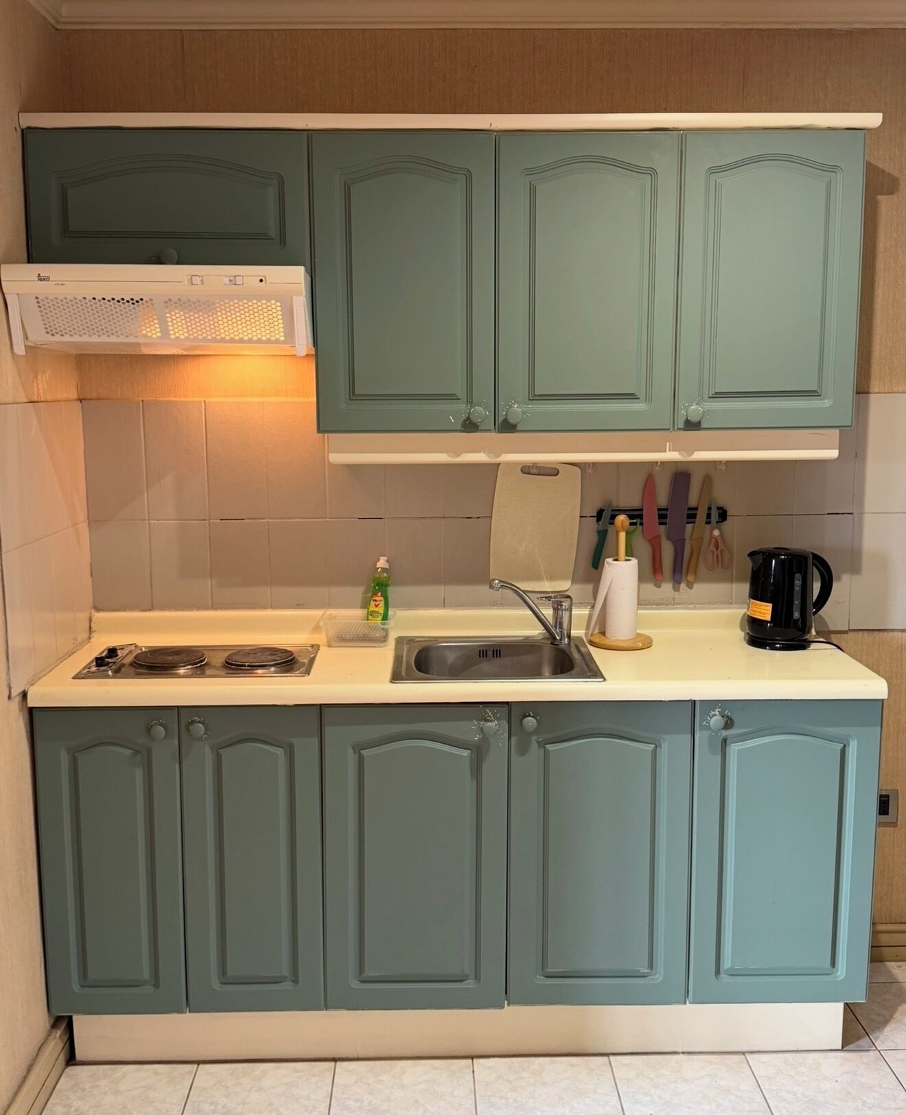 Una cocina con gabinetes color turquesa, una estufa, un lavamanos y diversos utensilios de cocina.