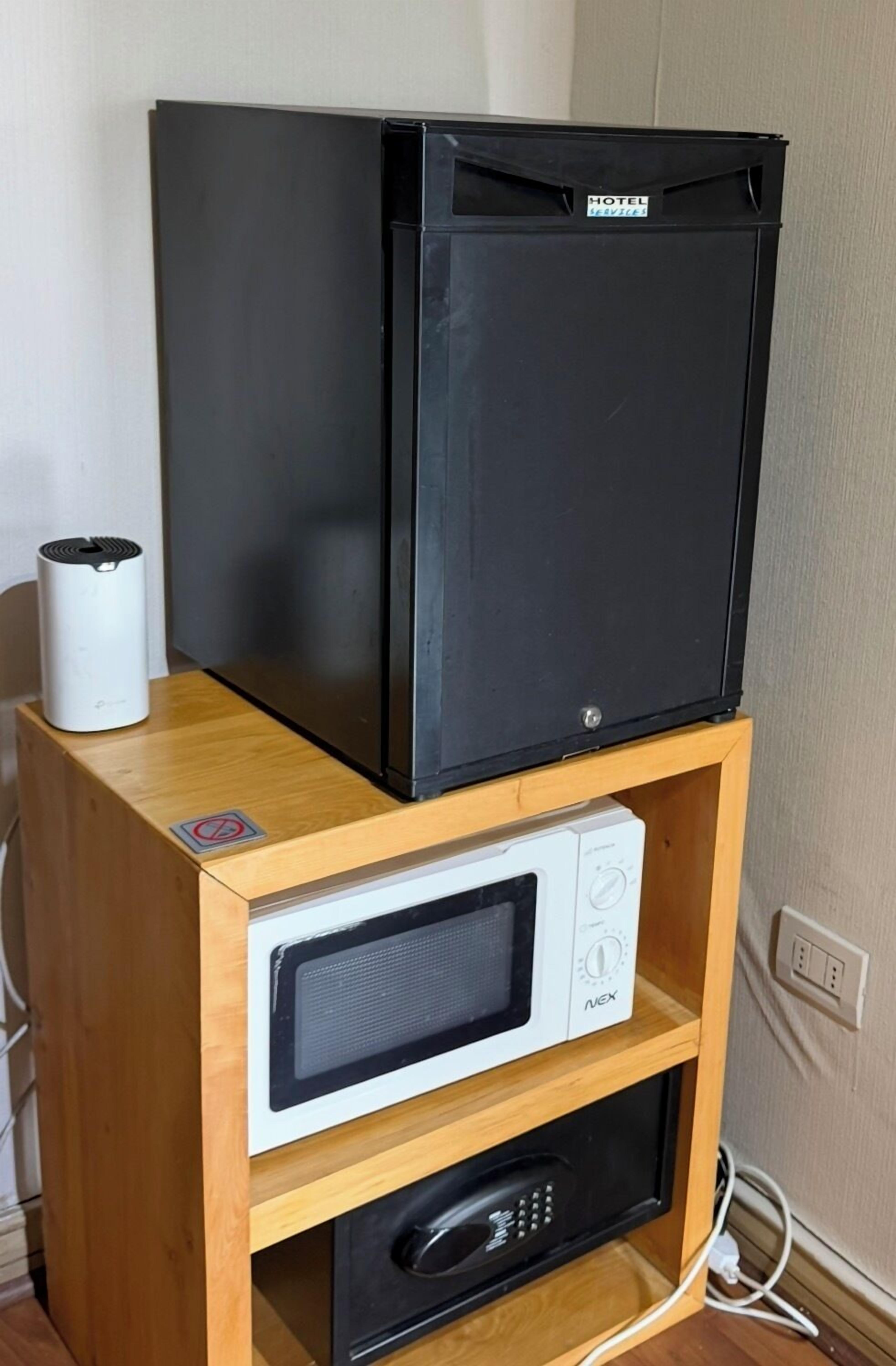A black refrigerator on a wooden cabinet with a white microwave below it.