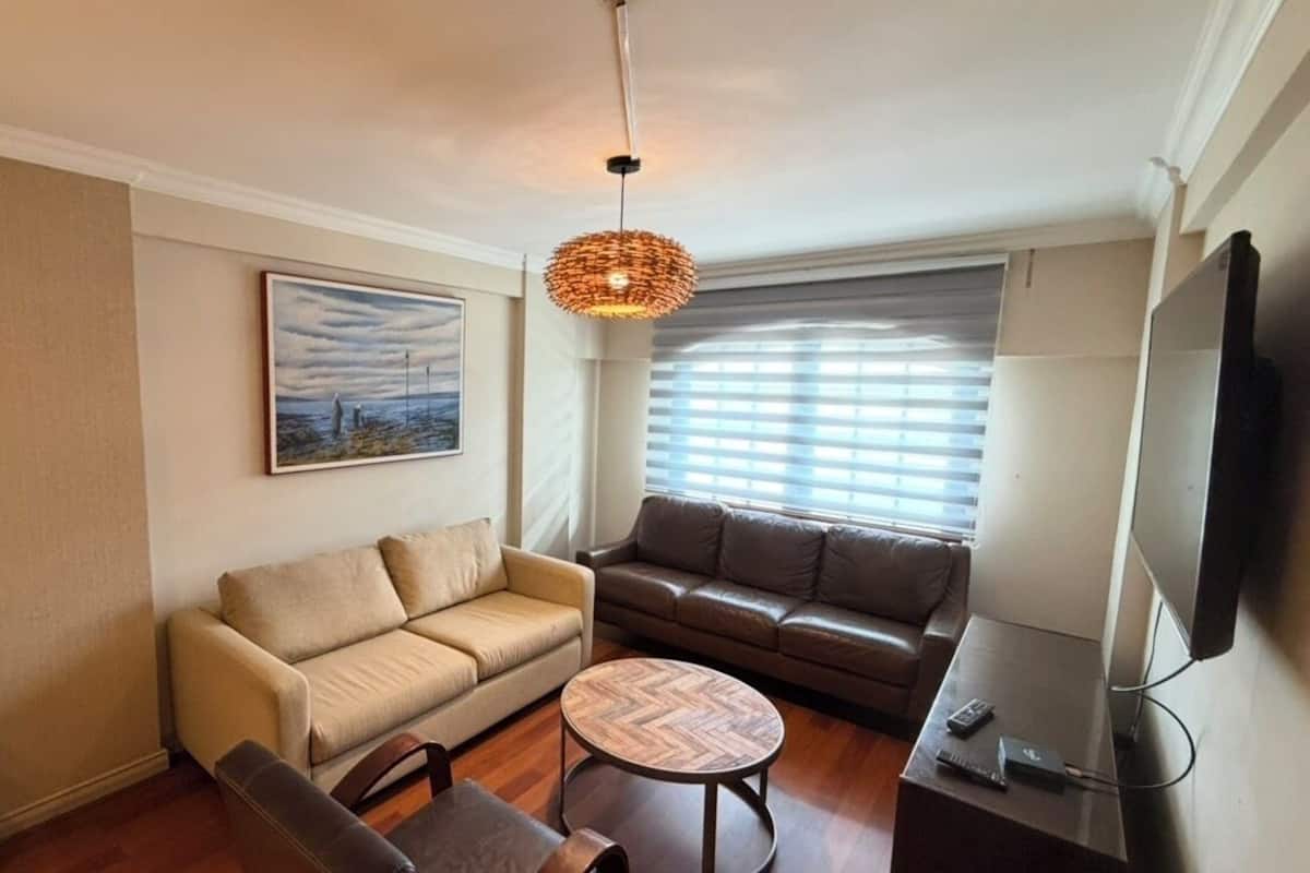 Ein Wohnzimmer mit Sofa, Sessel, Couchtisch, Fernseher und Kunstwerk an der Wand.