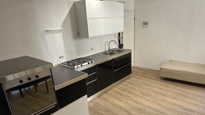 Una cocina compacta con estufa a gas, armarios negros, encimera blanca y un lavamanos pequeño.