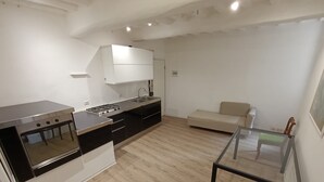 Una cocina moderna con estufa, lavaplatos y armarios, una mesa de comedor de vidrio y un sofá beige en la sala.