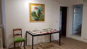 Una habitación con piso de madera, una silla verde acolchada, una mesa con estampado floral y un cuadro de temática tropical en la pared.