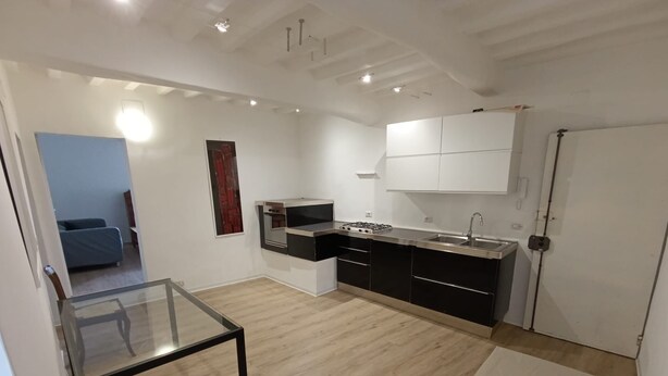 Cocina moderna con armarios blancos y negros, horno empotrado y pileta de acero inoxidable. En primer plano, una mesa de vidrio con una silla verde.