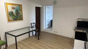 Una habitación con suelo de madera, una mesa de vidrio, una silla, un cuadro y una kitchenette.