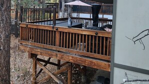 En stuga i två våningar med en träveranda, utomhusmöbler och en liten veranda.