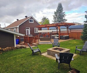 A backyard with a wooden deck, outdoor seating, and a fire pit. - Home Away From Home! (Timmins)