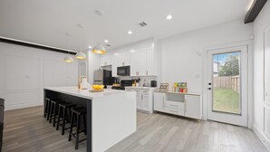 A modern kitchen with white cabinetry, a central island with bar stools, and pendant lighting.