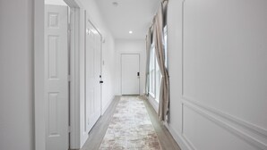 A hallway with white walls, a patterned rug, and a door at the end.