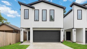 A modern two-story house with a garage, a wooden fence, and a clear blue sky.