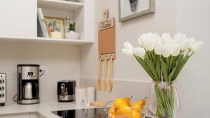 A kitchen with a coffee maker, a bowl of fruit, and a vase of flowers on the counter.
