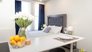 A modern hotel room with a bed, bedside table, and a dining area.