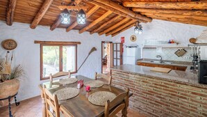 A rustic kitchen with a brick island, wooden ceiling beams, and a dining area with woven placemats. - Cozy Paradise El Gastor by Ruralidays (Cádiz)