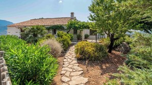 A stone pathway leading to a house with a tiled roof, surrounded by various shrubs and trees. - Cozy Paradise El Gastor by Ruralidays (Cádiz)