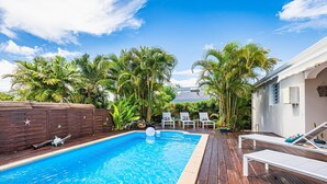 A swimming pool with wooden deck, lounge chairs, and tropical plants. - Villa Blue Cane with a pool and ping-pong table, perfect for families (Le MOULE)