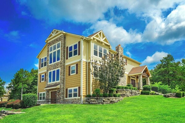 A multi-story house with a stone facade, large windows, and a well-maintained lawn. - Sleeps 18 | 6BR Branson Lodge – Pool, Hot Tub & Game Room (Hollister)
