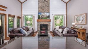 A spacious living room with a stone fireplace, leather sofas, and a glass coffee table. - Branson Retreat Lodge – Hot Tub, Pools & Game Room (Hollister)