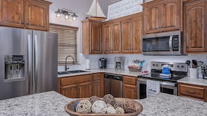A kitchen with wooden cabinets, stainless steel appliances, a granite countertop, and a decorative bowl. - Branson Retreat Lodge – Hot Tub, Pools & Game Room (Hollister)