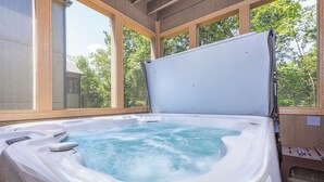 A hot tub with a wooden deck and large windows, surrounded by trees. - Branson Retreat Lodge – Hot Tub, Pools & Game Room (Hollister)