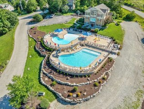 Une grande piscine circulaire dotée d’une fontaine centrale, entourée d’espaces de détente et avec un bâtiment visible au loin.