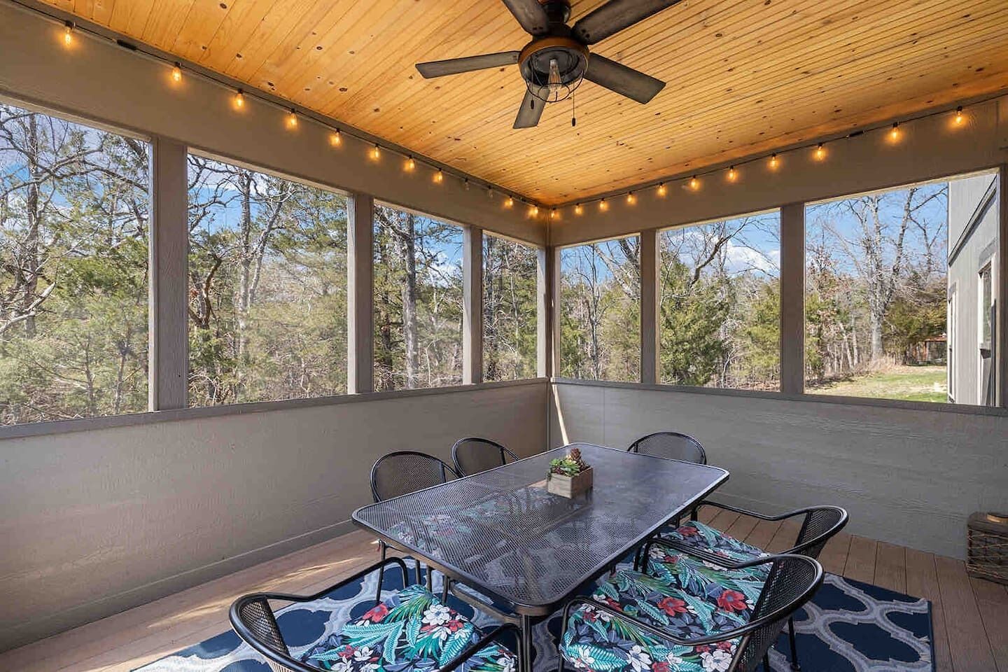 A covered patio with a table and chairs, large windows, and a ceiling fan.