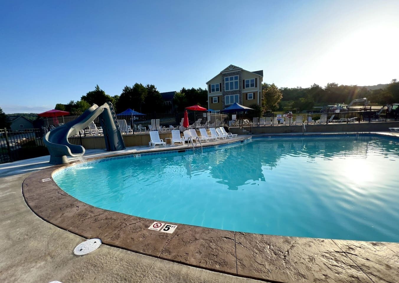 Una piscina con tobogán, sillas de descanso, sombrillas y un edificio al fondo.