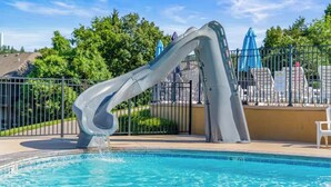 Une piscine avec un toboggan, entourée d’une clôture et de chaises longues.