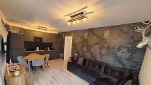 Een moderne woonkamer met een donker leren bank, een houten eettafel met stoelen, en een keuken met een marmeren achterwand.
