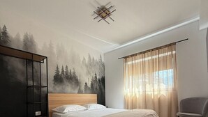 Een slaapkamer met een bed, hoofdbord, kast, stoel en een raam met gordijnen.