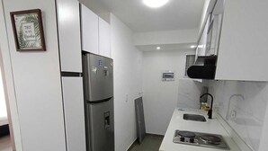Una cocina compacta con armarios blancos, un refrigerador de acero inoxidable, horno integrado y un lavamanos.