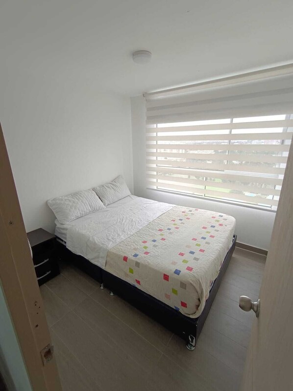 Une chambre à coucher avec un lit, une fenêtre avec des stores et une porte.