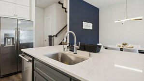Una cocina moderna con un refrigerador de acero inoxidable, una encimera blanca, un fregadero y una pared de acento azul oscuro.