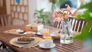 Une table de salle à manger en bois, mise pour le petit-déjeuner, avec un saladier de fruits, une assiette de croissants, un verre de jus d’orange et une tasse blanche.
