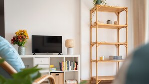Un salon avec un téléviseur, une bibliothèque et une étagère en osier.
