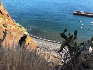 A coastal landscape with a rocky shoreline, clear blue water, and sparse vegetation. - Casa da Maresia - The Seaside Escape (Paúl do Mar)