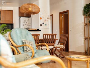 Un salon comprenant un canapé, des fauteuils, une table à manger et un coin cuisine avec un réfrigérateur, ainsi qu’un luminaire suspendu.