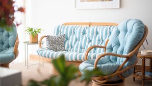 Une pièce avec un canapé à rayures, un fauteuil en osier, une petite table sur laquelle est posée une plante, et un tableau encadré accroché au mur.