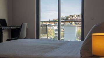 Une chambre d’hôtel équipée d’un lit, d’un bureau avec un ordinateur portable, d’une chaise et d’une grande fenêtre donnant sur la ville.