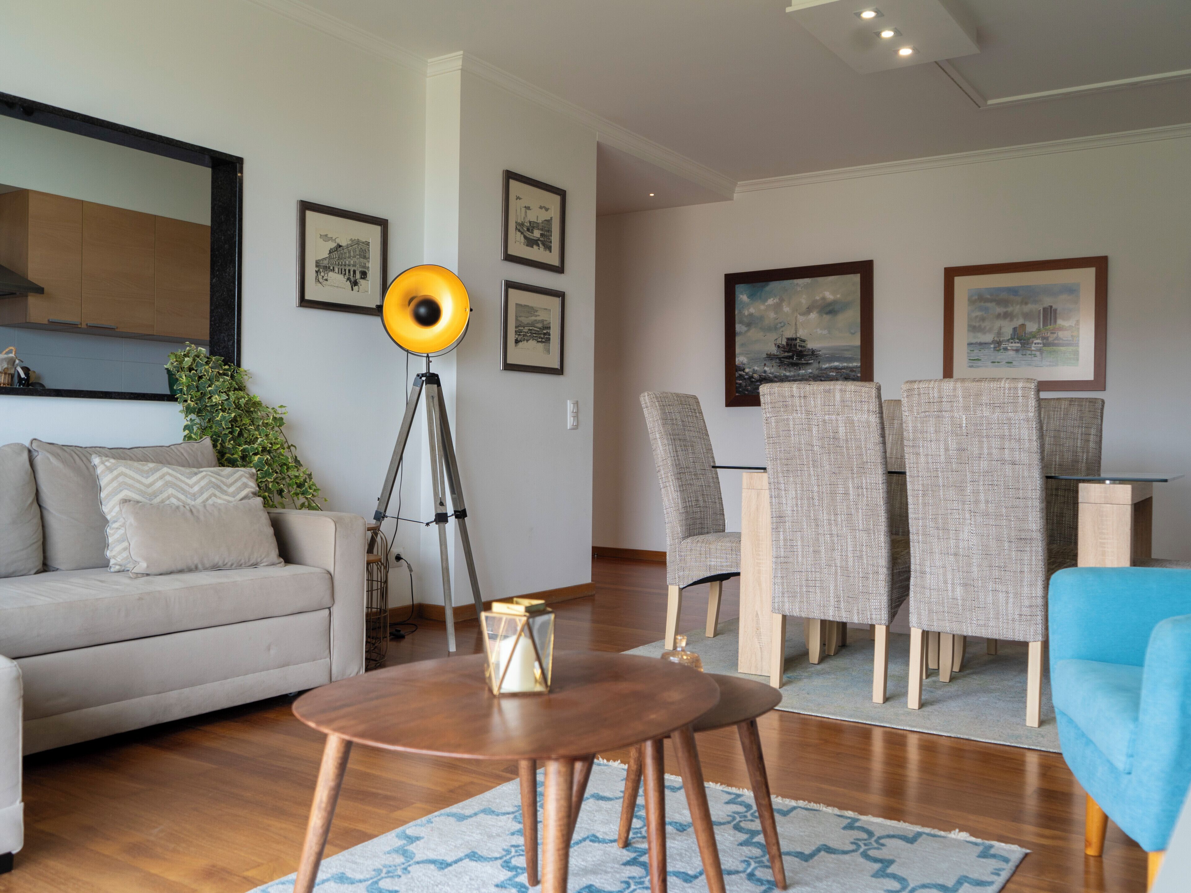 Un salon moderne comprenant un canapé, une table à manger avec des chaises, une lampe sur pied et des œuvres d’art encadrées accrochées aux murs.