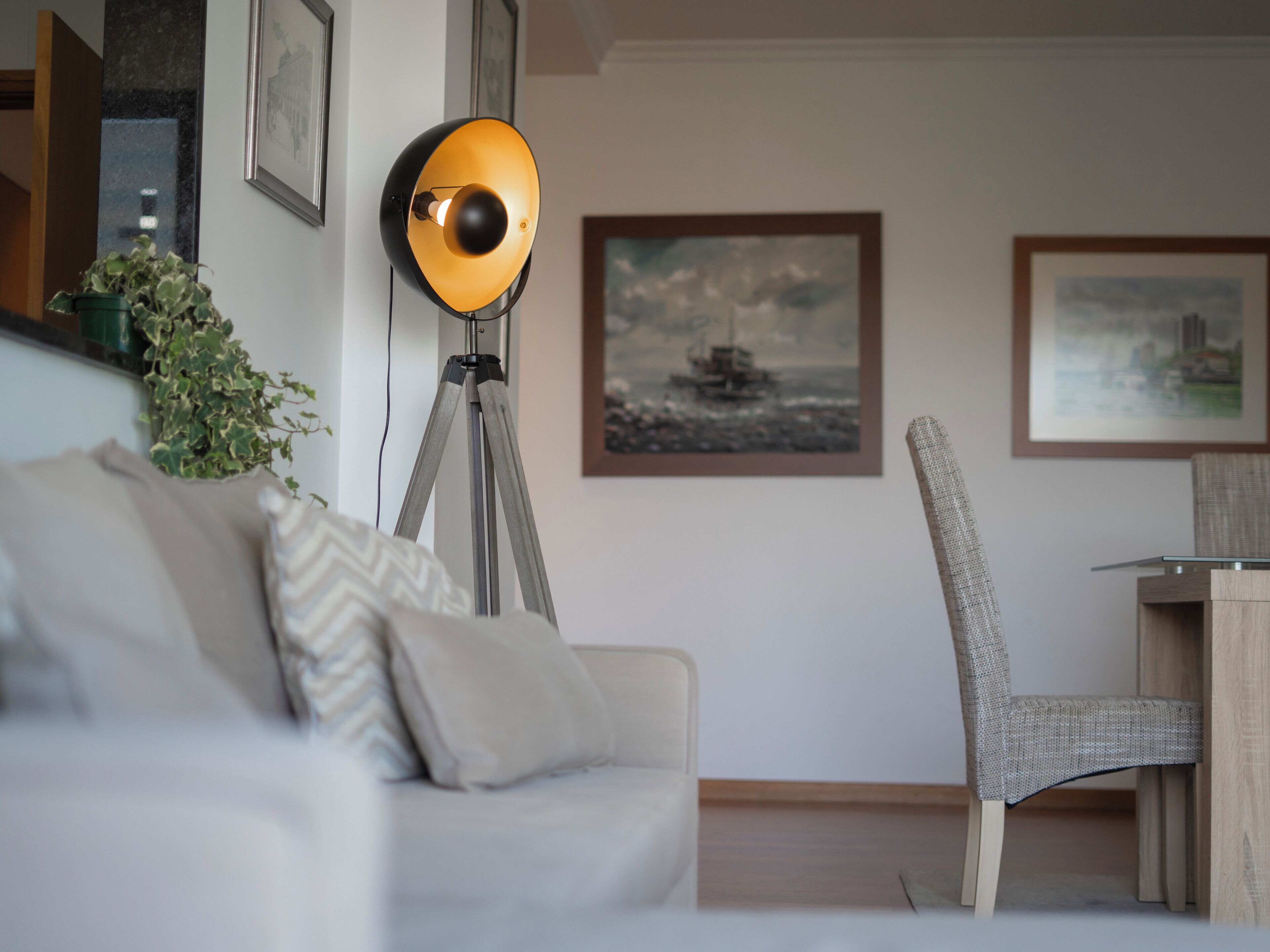 Un salon moderne avec un canapé, une lampe sur pied, un fauteuil et des œuvres d’art encadrées accrochées au mur.