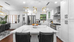 A modern kitchen with white cabinetry, a large island with a marble countertop, and pendant lighting. - Lux•PrimeLocation•HtdResortPool•OutdrDining (West Palm Beach)