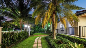 A well-maintained garden with a stone pathway, palm trees, and a neatly trimmed hedge. - Lux•PrimeLocation•HtdResortPool•OutdrDining (West Palm Beach)