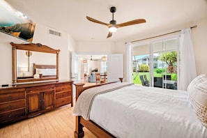 Une chambre à coucher avec un lit, une commode en bois, un ventilateur de plafond et une grande fenêtre avec des rideaux.