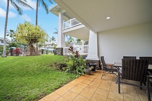 Un patio couvert aménagé avec du mobilier d’extérieur, une pelouse bien entretenue et une vue sur un quartier résidentiel avec des maisons et des palmiers.