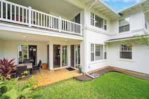 A two-story house with a balcony, a patio with a table and chairs, and a well-maintained lawn.
