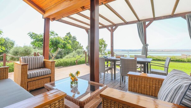 An outdoor patio with wicker furniture, a glass table, and a view of the sea. - Finca Mis Morenas Moguer by Ruralidays (Huelva)