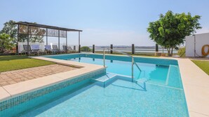 A rectangular swimming pool with a tiled deck area, a covered seating area with chairs, and a tree in the background. - Finca Mis Morenas Moguer by Ruralidays (Huelva)
