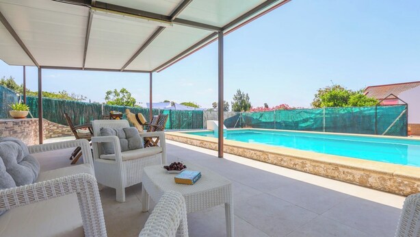 A covered outdoor area with wicker furniture, a pool, and a view of the surrounding area.