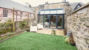 A stone house with a glass conservatory, a grassy yard, and a white chair.