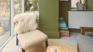A cozy room with a stone wall, a large window, a fluffy chair, a wooden table, and a potted plant.