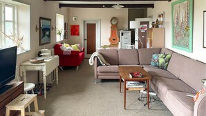 A cozy living room with a red sofa, a brown sofa, a wooden coffee table, and a television. There is a white table with a vase and a clock on the wall.